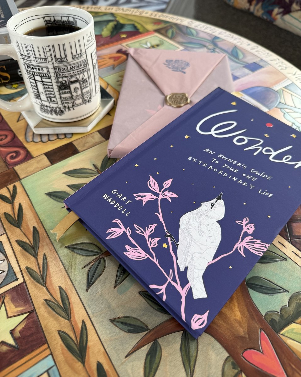 A hardcover of Wonder and its wrapped package on a painted table beside a cup of coffee
