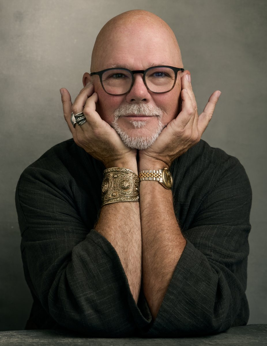 Gary Waddell resting his chin in both hands, smiling gently, wearing a gold cuff